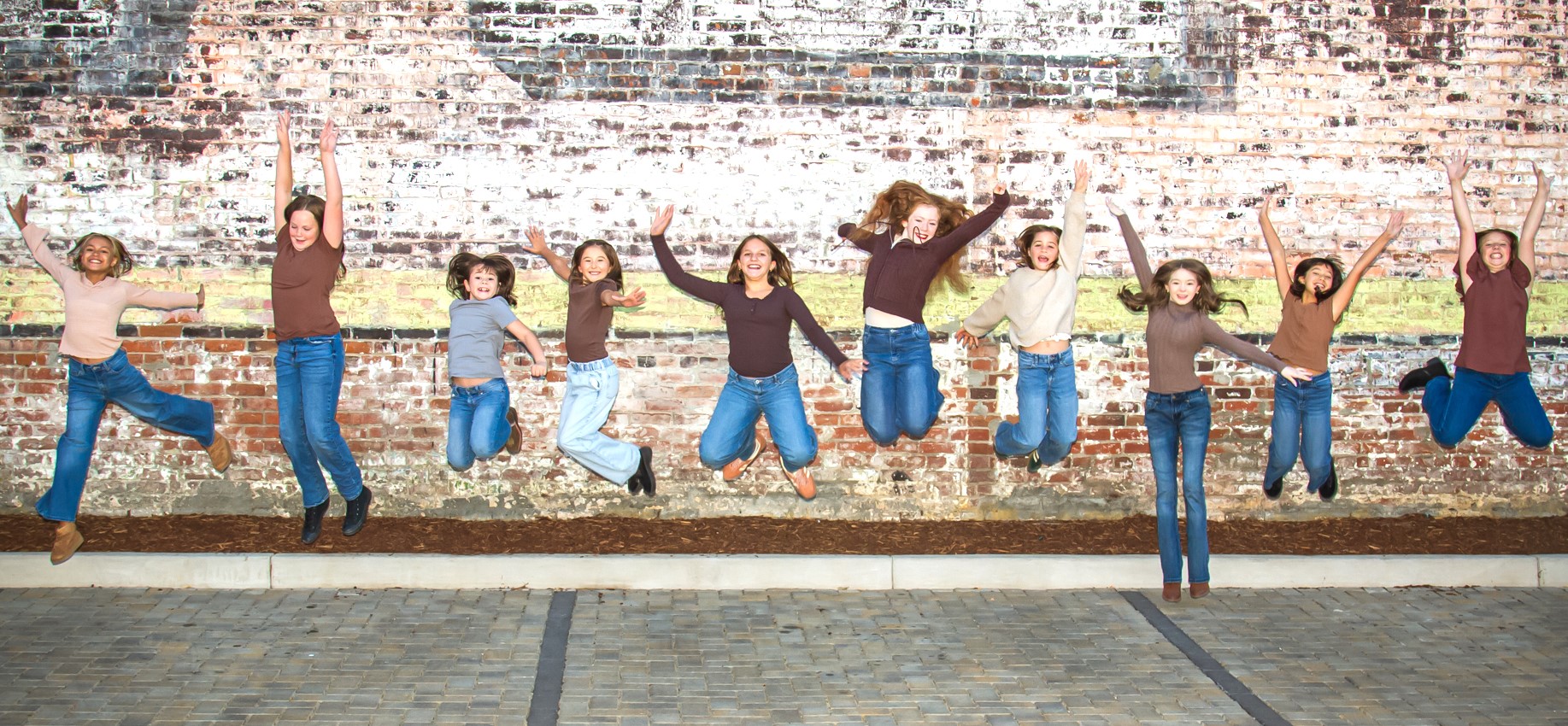 SODC dancers jumping together in front of a brick wall